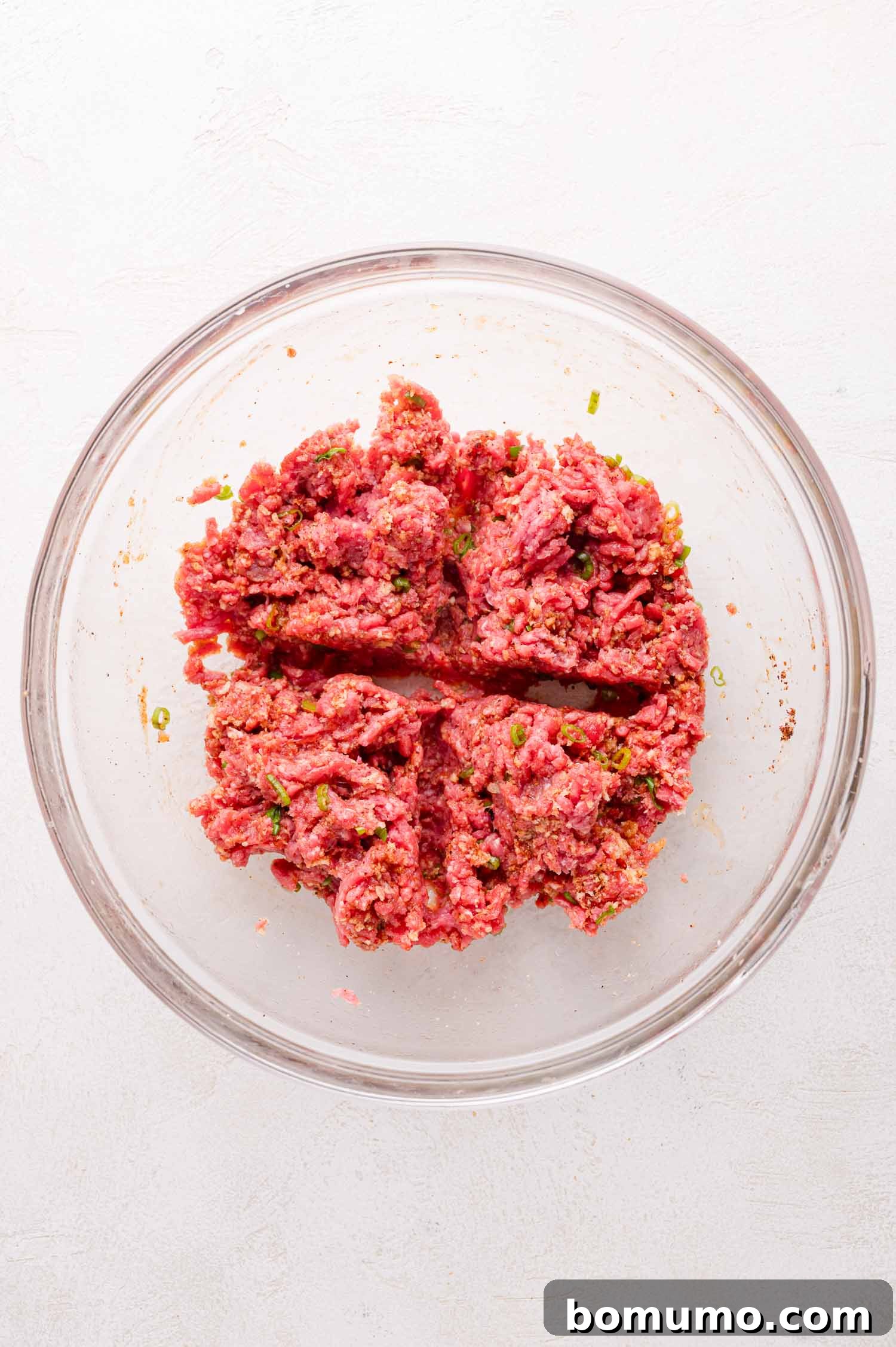 Sheet Pan BBQ Mini Meatloaves 9 Ground beef mixture with herbs and spices in a glass bowl, divided into four sections.