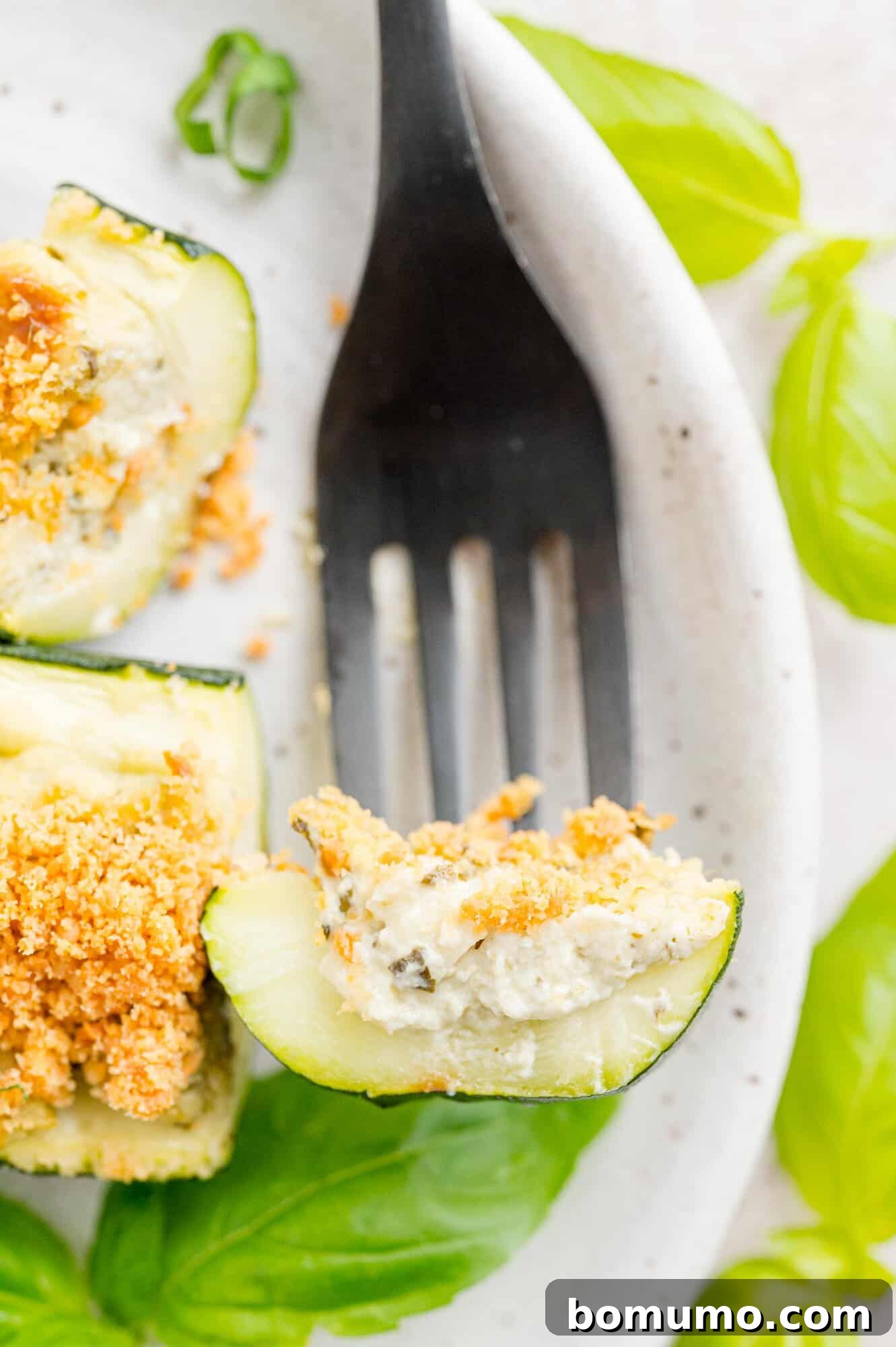 A single piece of cheese and pesto stuffed zucchini on a fork, showing the delicious filling.
