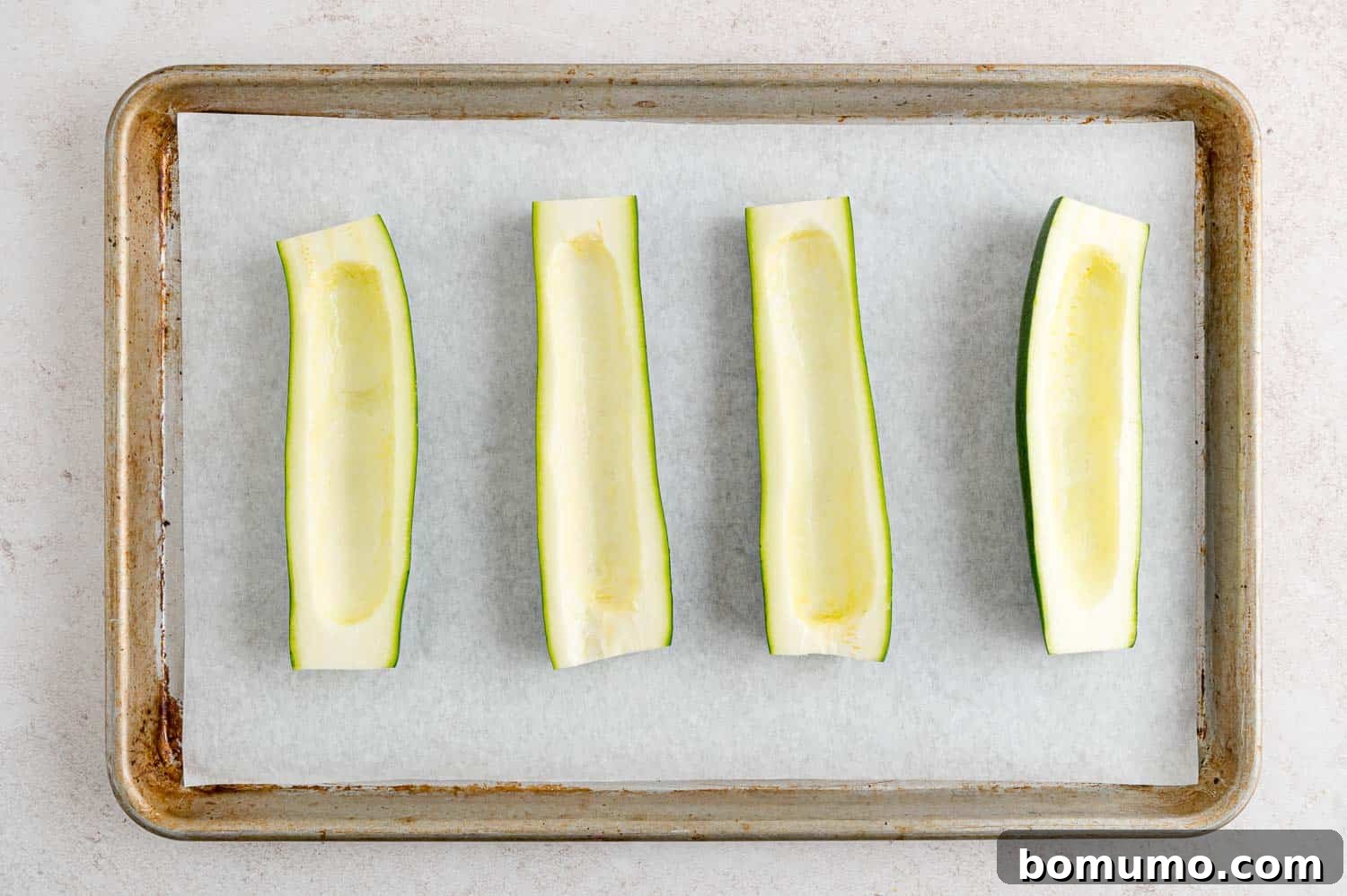 Hollowed-out zucchini halves neatly arranged on a baking sheet, ready for filling.