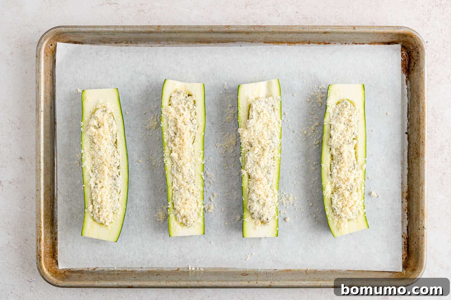 Zucchini halves generously filled with the cheese and pesto mixture, before being baked.