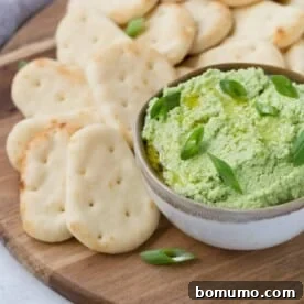 A small white bowl filled with bright green edamame dip, beautifully garnished with fresh green onions, ready for dipping.