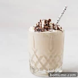 A decadent maple whiskey milkshake, expertly topped with a generous swirl of whipped cream and a luscious drizzle of chocolate syrup, served with a fun striped straw.