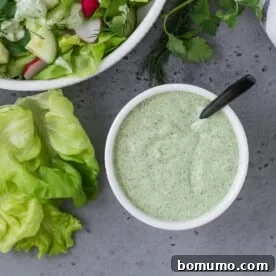 An overhead shot of vibrant green goddess dressing in a small white bowl, showcasing its fresh, herby texture and appealing color.