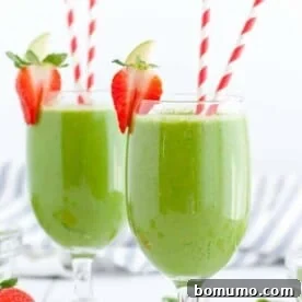 Two refreshing green smoothies served in elegant stemmed glasses, beautifully garnished with fresh strawberries and whimsical red and white straws.