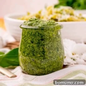 A glass jar brimming with vibrant, homemade basil pesto, ready to enhance a variety of culinary creations with its fresh, aromatic flavor.