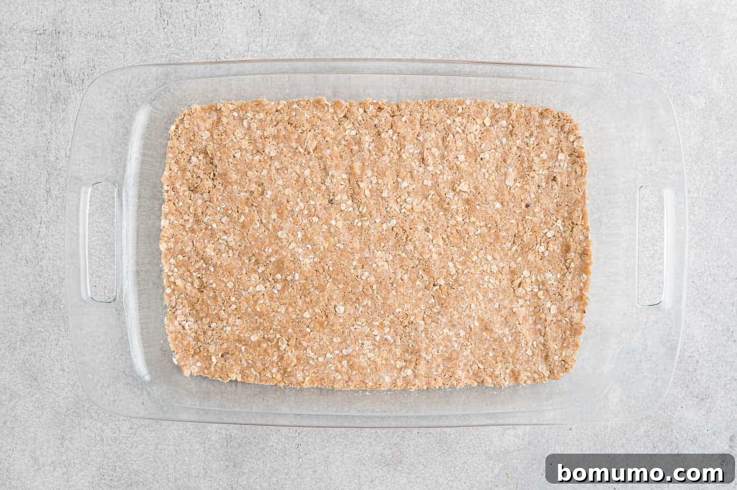 The crumbly mixture being pressed into the bottom of the prepared baking pan.