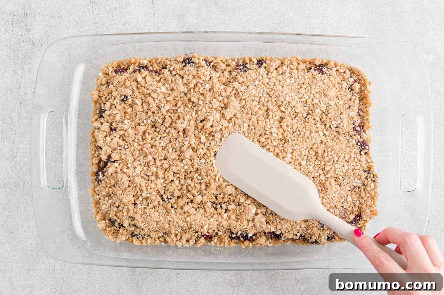 The reserved crumbly mixture being sprinkled over the blueberry filling for the final layer.