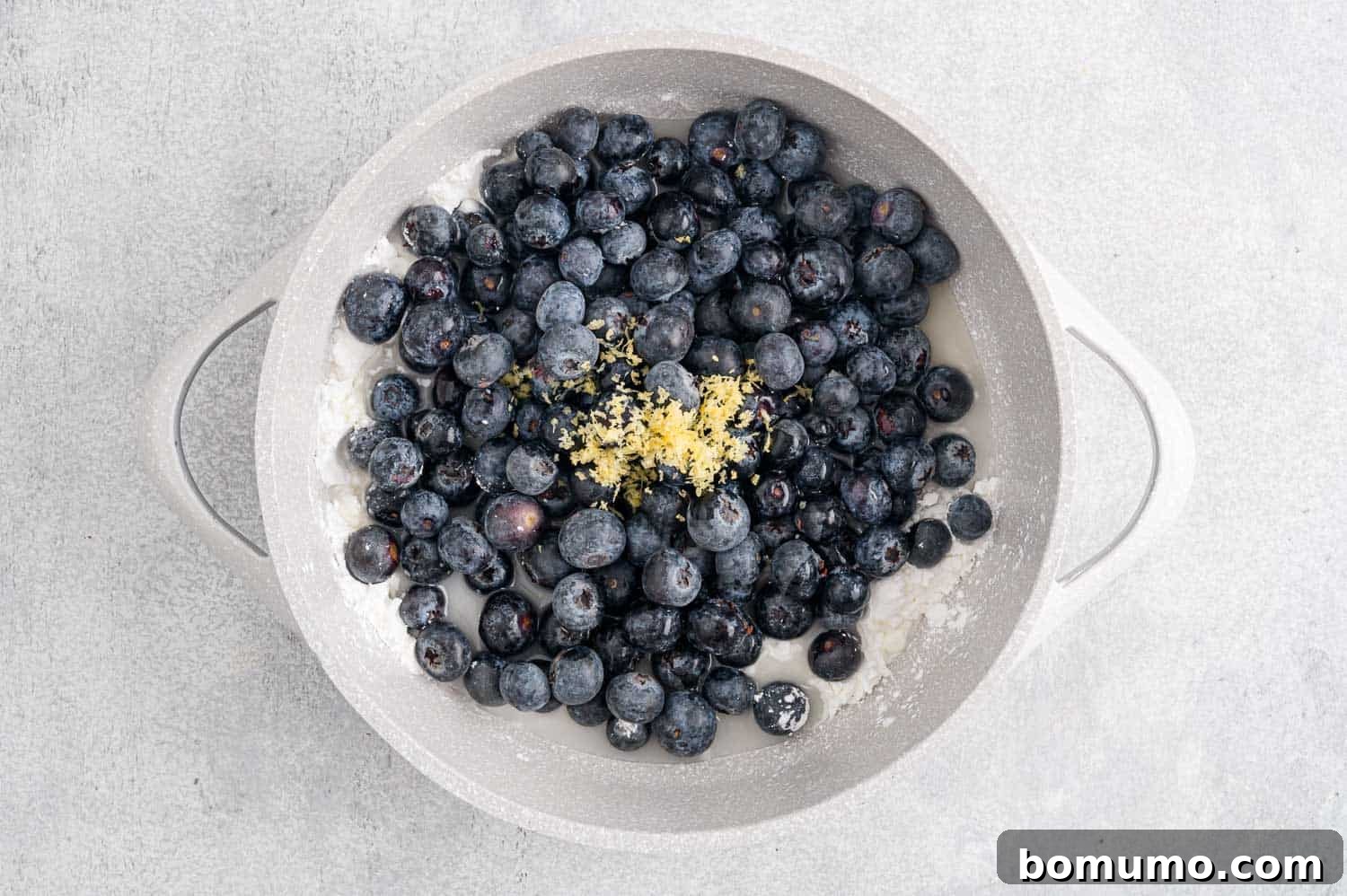 Sugar, cornstarch, blueberries, lemon juice, lemon zest, and water being added to a saucepan.