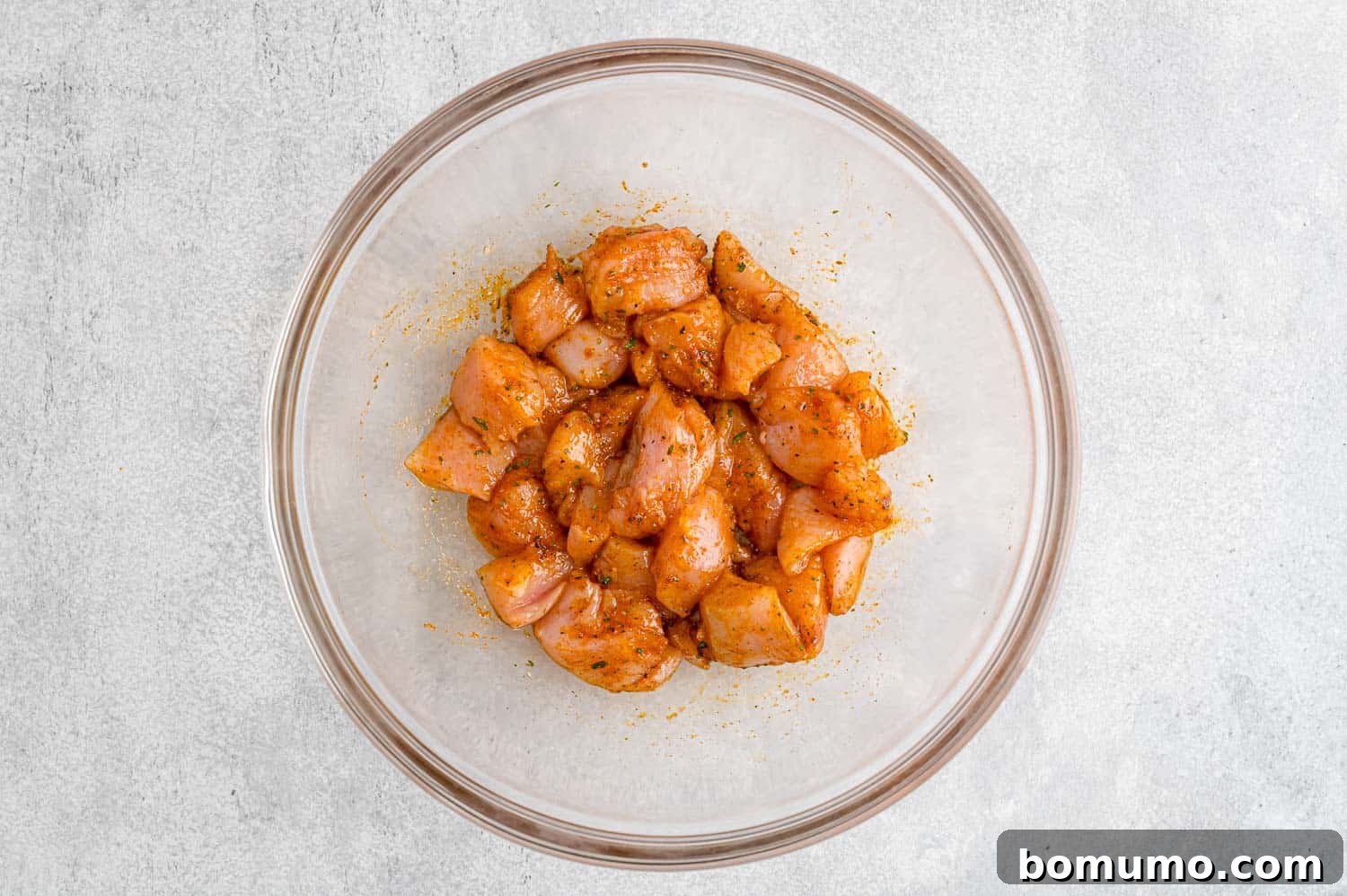 Diced raw chicken pieces thoroughly coated in a vibrant blend of spices and olive oil, glistening in a mixing bowl, perfectly seasoned and ready to join the vegetables on the sheet pan.