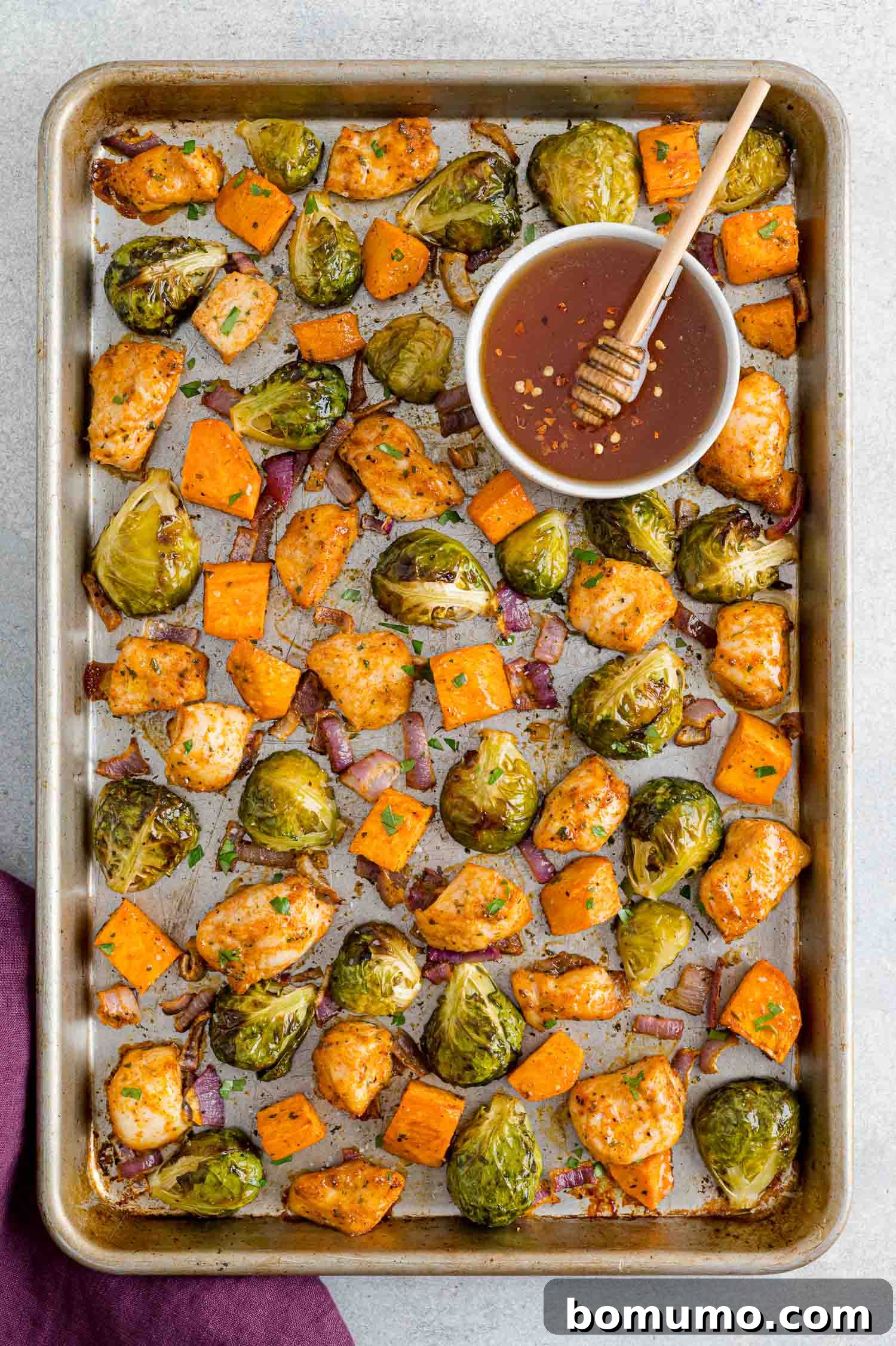 A close-up image of the completed Hot Honey Chicken Sheet Pan Dinner on a white plate, featuring perfectly golden chicken, charred Brussels sprouts, and tender sweet potatoes, all beautifully glazed and ready to eat.