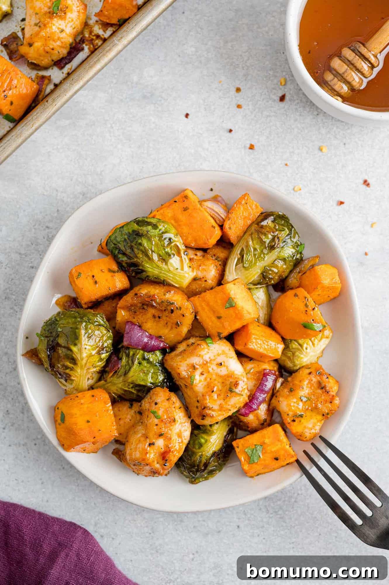 A single, artfully plated serving of hot honey chicken, roasted Brussels sprouts, and sweet potatoes on a small white plate, showcasing the vibrant colors and appealing texture of the finished dish.