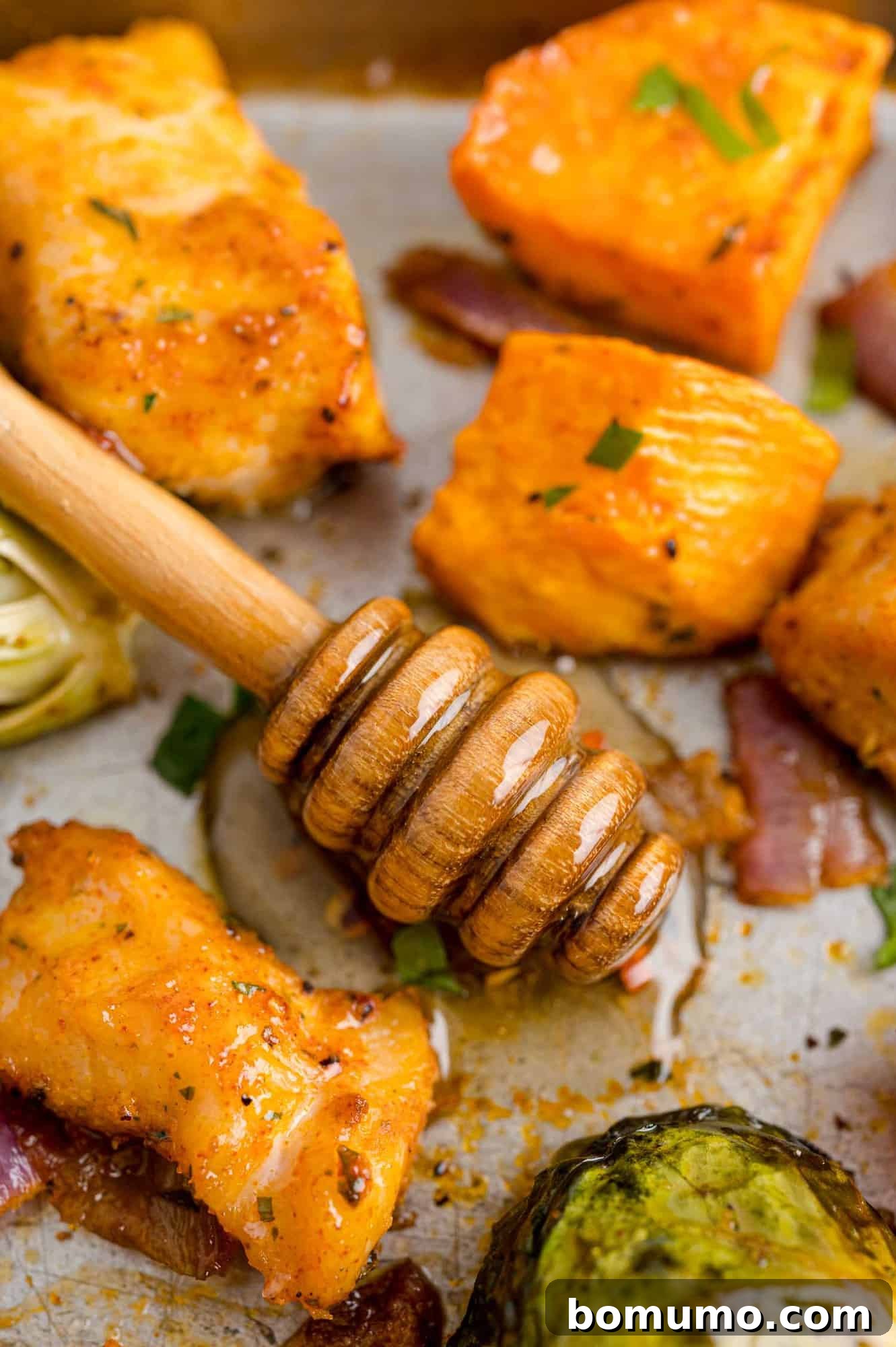 A generous drizzle of vibrant hot honey cascading over a sheet pan filled with beautifully roasted Brussels sprouts, golden-brown chicken, and tender sweet potatoes, creating an appetizing, glossy finish.