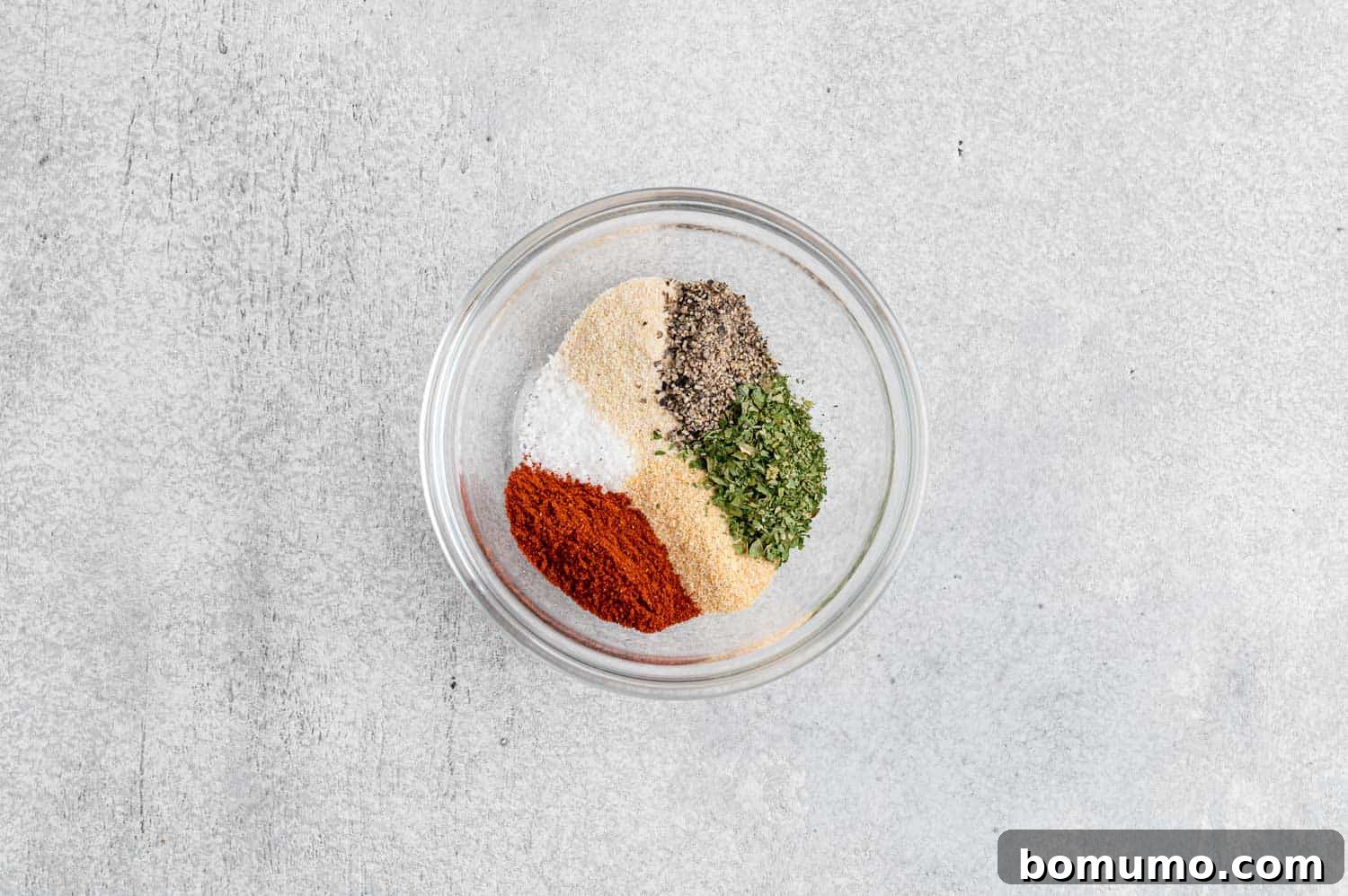A selection of unmixed dry seasoning ingredients, including red pepper flakes, garlic powder, and paprika, artfully arranged in small, individual mounds on a clean white surface, awaiting their combination into a unified blend.
