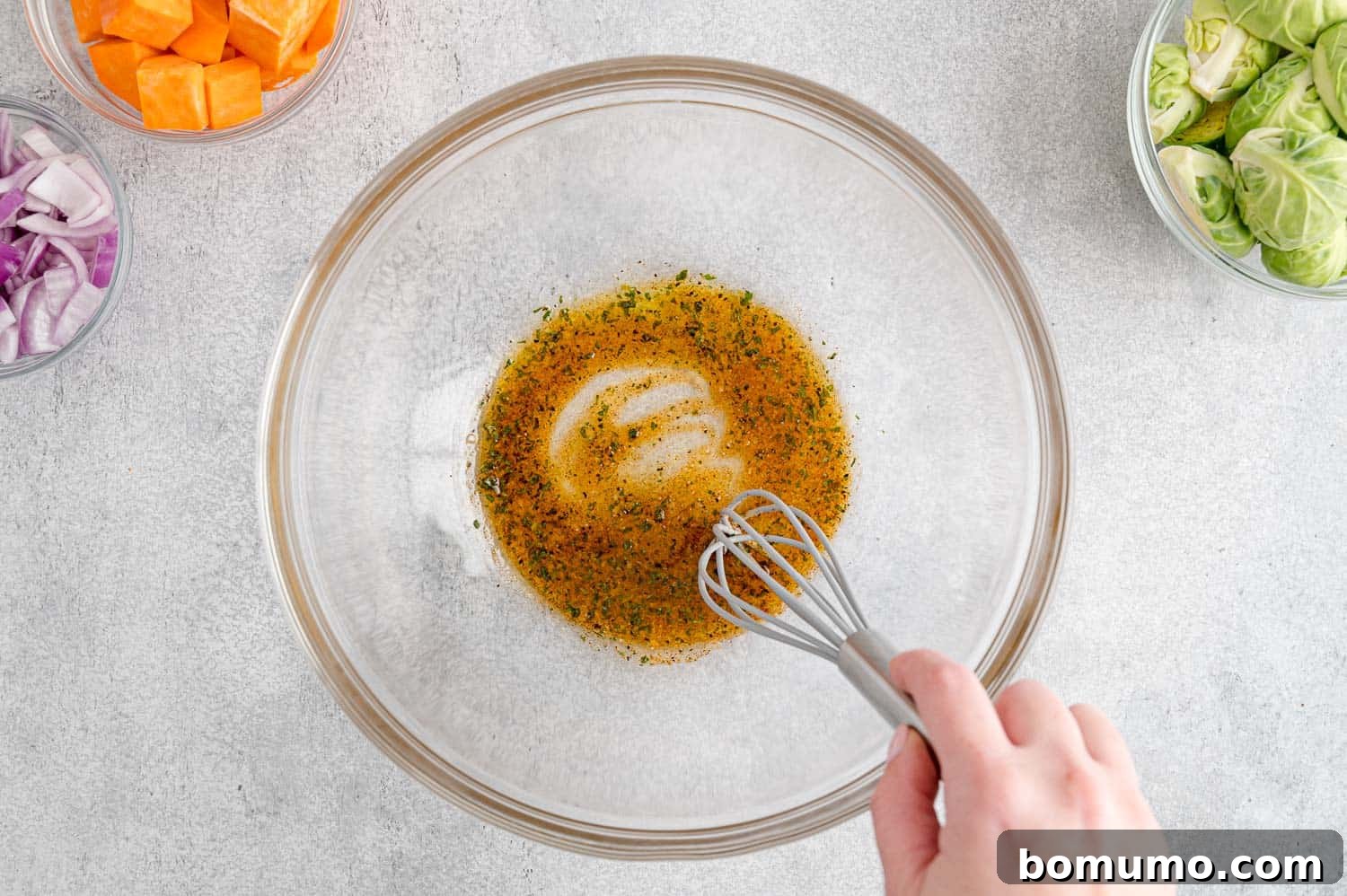 A close-up, overhead shot revealing a rich mixture of olive oil expertly blended with an aromatic array of dried seasonings in a spacious white mixing bowl, forming a fragrant paste ready to generously coat the ingredients.