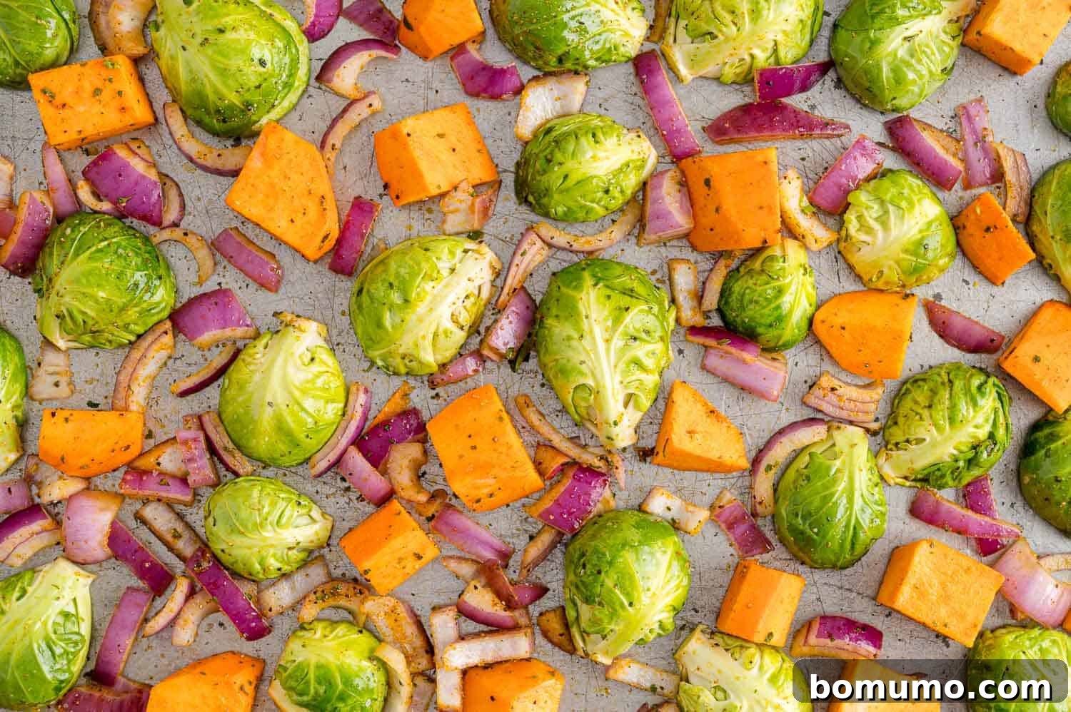 Raw, seasoned Brussels sprouts, sweet potatoes, and red onion meticulously arranged in a single, uncrowded layer on a sheet pan, perfectly poised for their first roast in the oven.