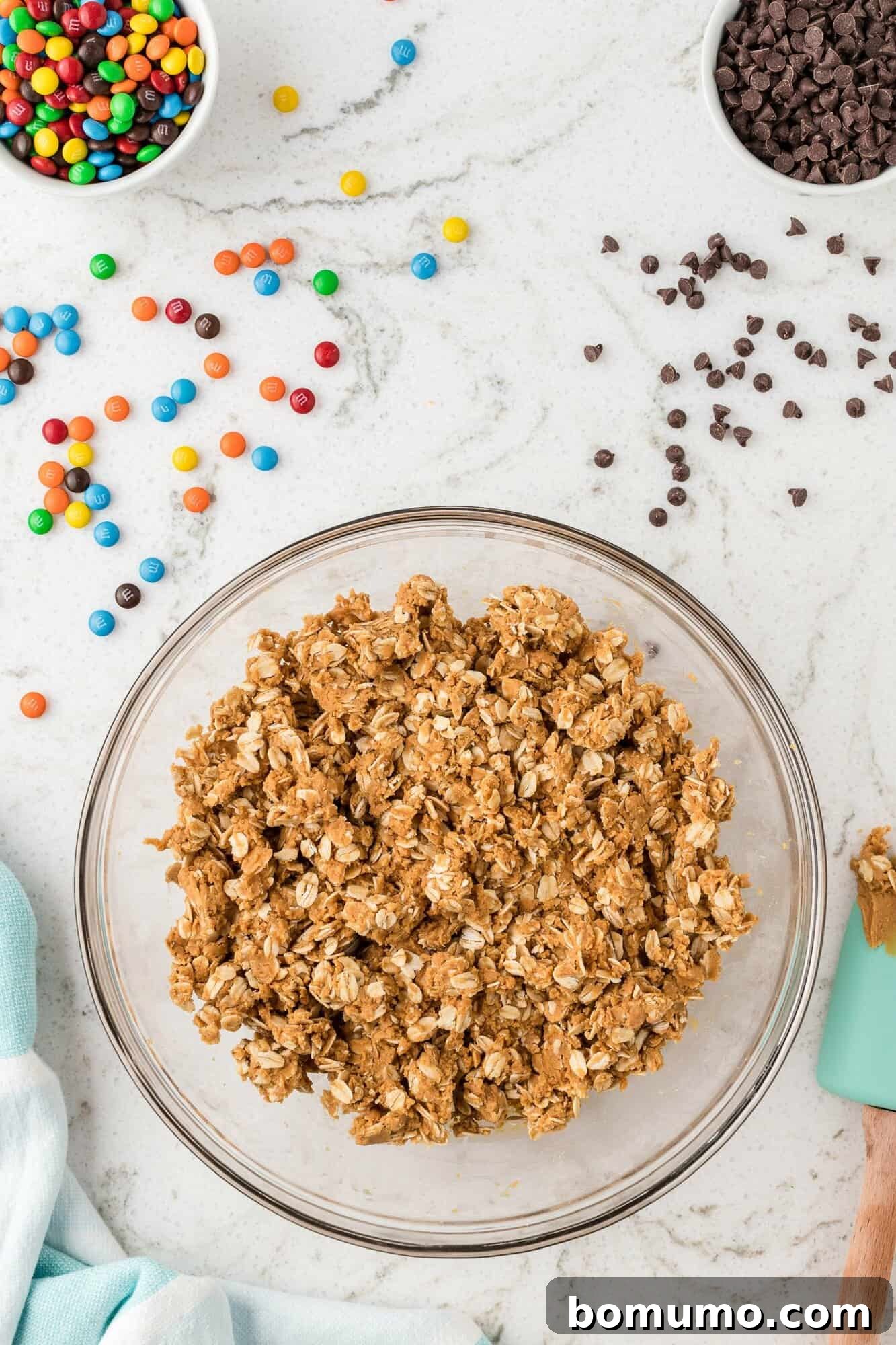 Close-up shot of rolled oats being expertly stirred into the thick peanut butter mixture in a mixing bowl, creating the base for the energy balls.