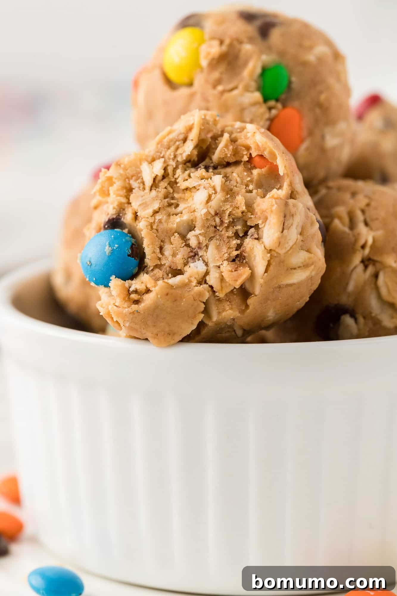 A Monster Cookie Energy Bite with a small bite taken out, revealing its rich interior of peanut butter, oats, chocolate chips, and colorful M&M's.