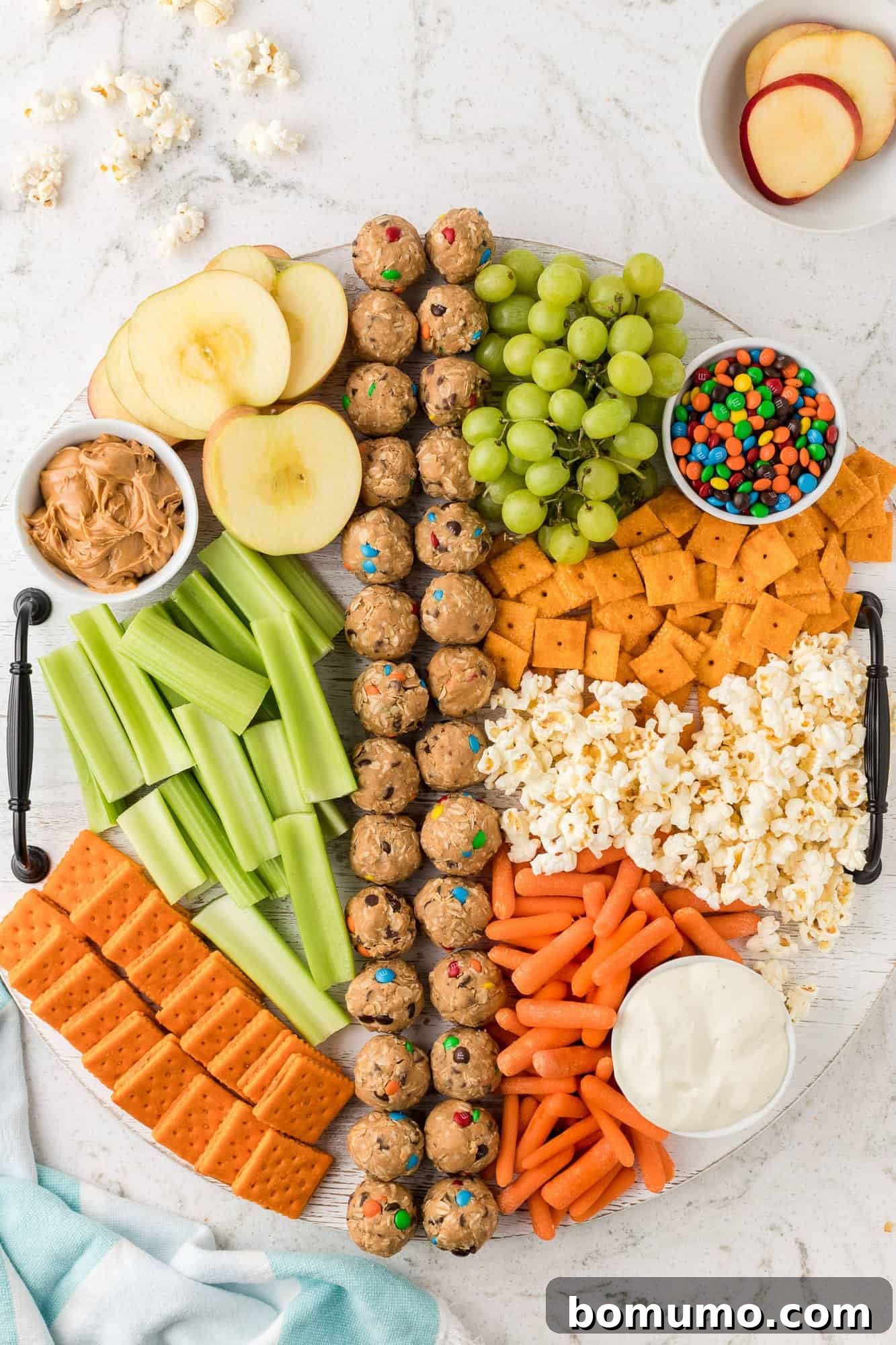 A completed snack board featuring carrots, celery, various crackers, and popcorn.