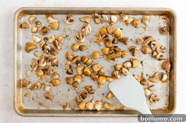Roasted White Mushrooms for Enhanced Flavor A white spatula stirring seasoned white mushrooms on a baking sheet, ready for roasting.