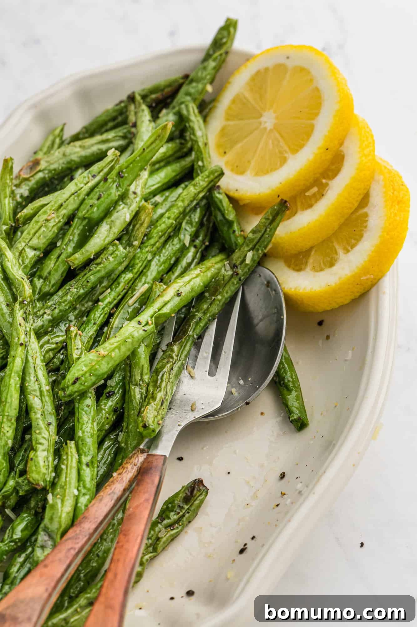 Perfectly air-fried green beans presented on a white platter, garnished with fresh lemon slices.