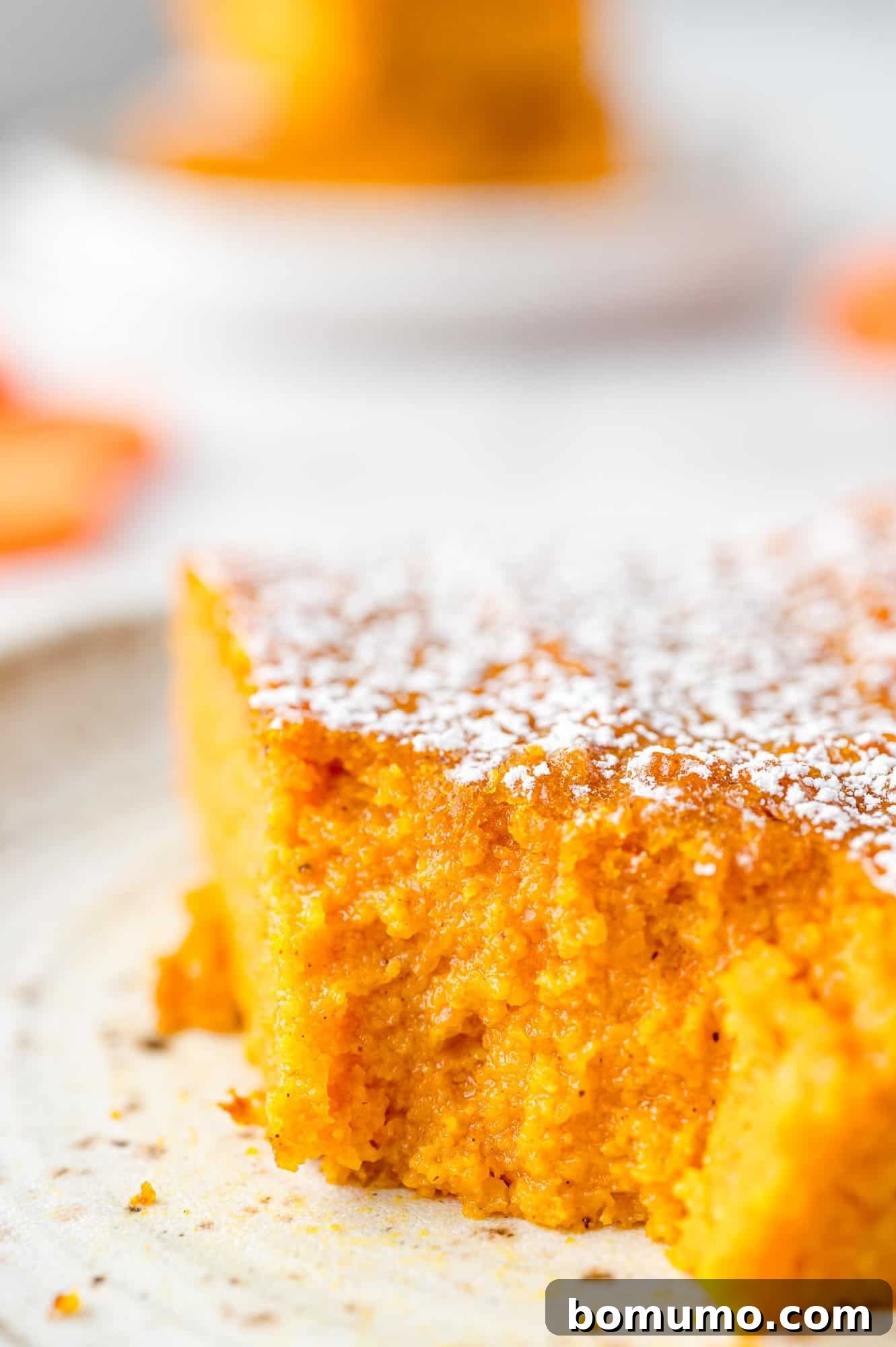 A perfectly portioned slice of golden-orange carrot soufflé, with a small forkful removed, resting on a white plate beside a silver fork.