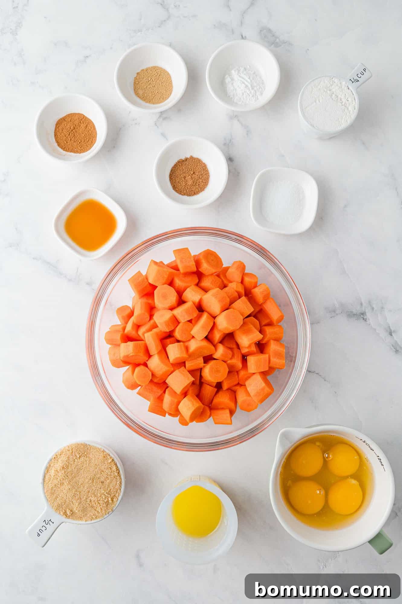 A collection of fresh ingredients laid out on a wooden surface, including peeled carrots, eggs, butter, brown sugar, flour, and a selection of spices, ready for making carrot soufflé.