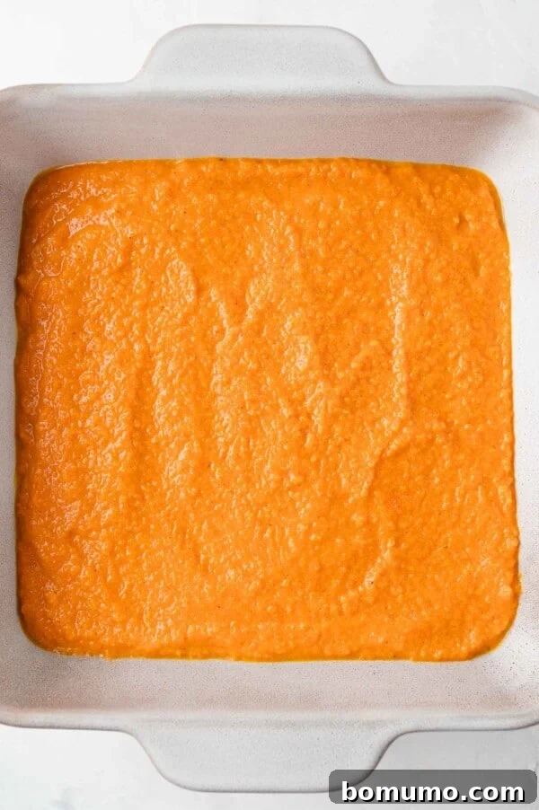 The smooth, orange carrot soufflé batter is evenly spread in a square ceramic baking dish, ready for baking.