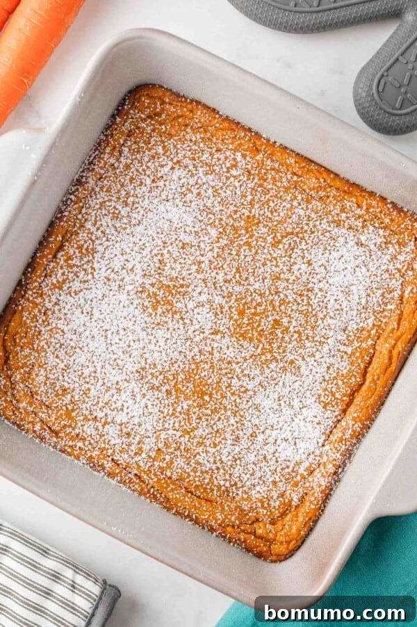 An overhead view of the freshly baked carrot soufflé in a ceramic baking dish, lightly dusted with powdered sugar, showcasing its golden-brown top.