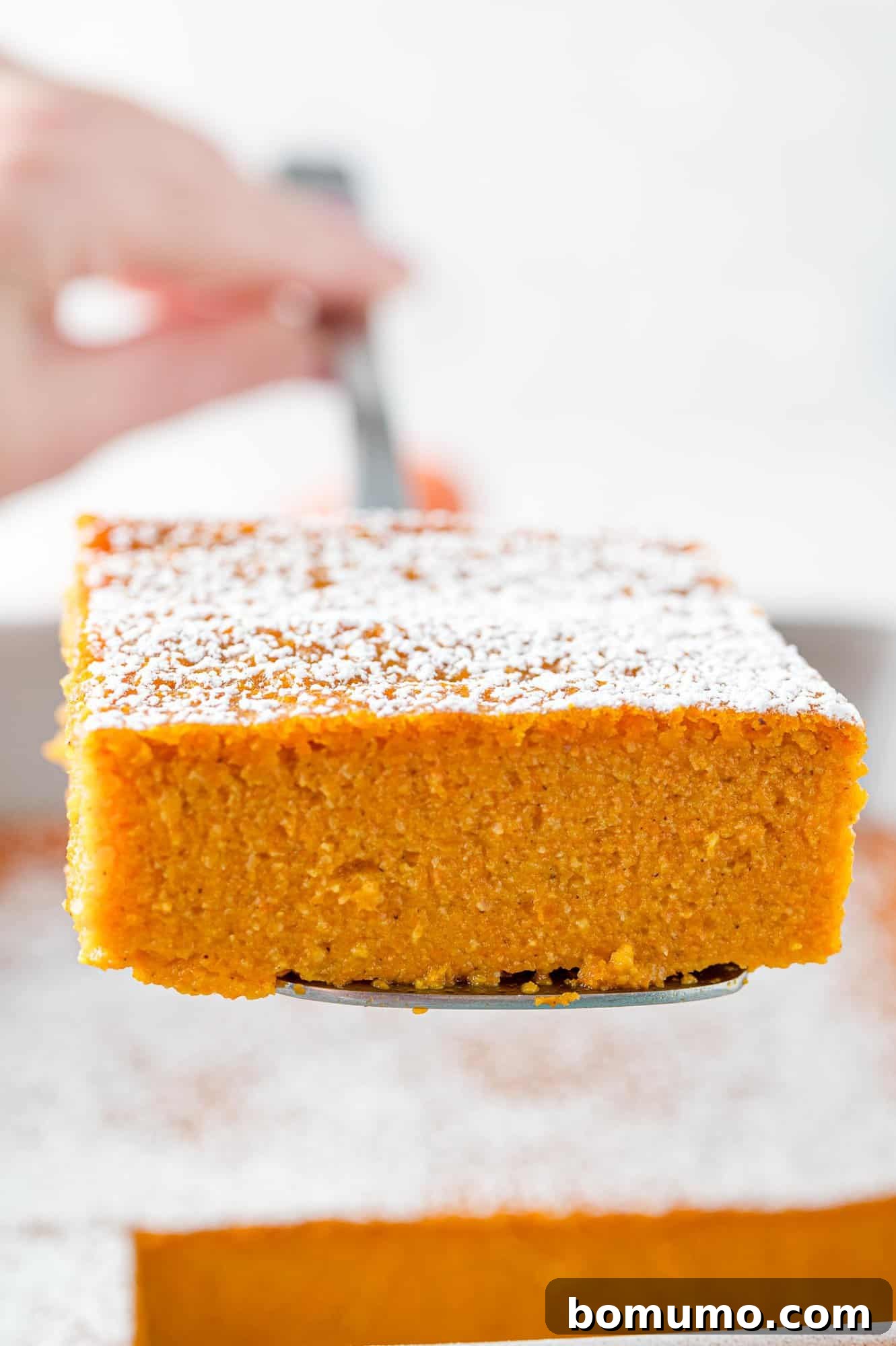 A close-up shot of a single slice of carrot soufflé, delicately lifted from the baking dish by a spatula, revealing its soft, fluffy interior.