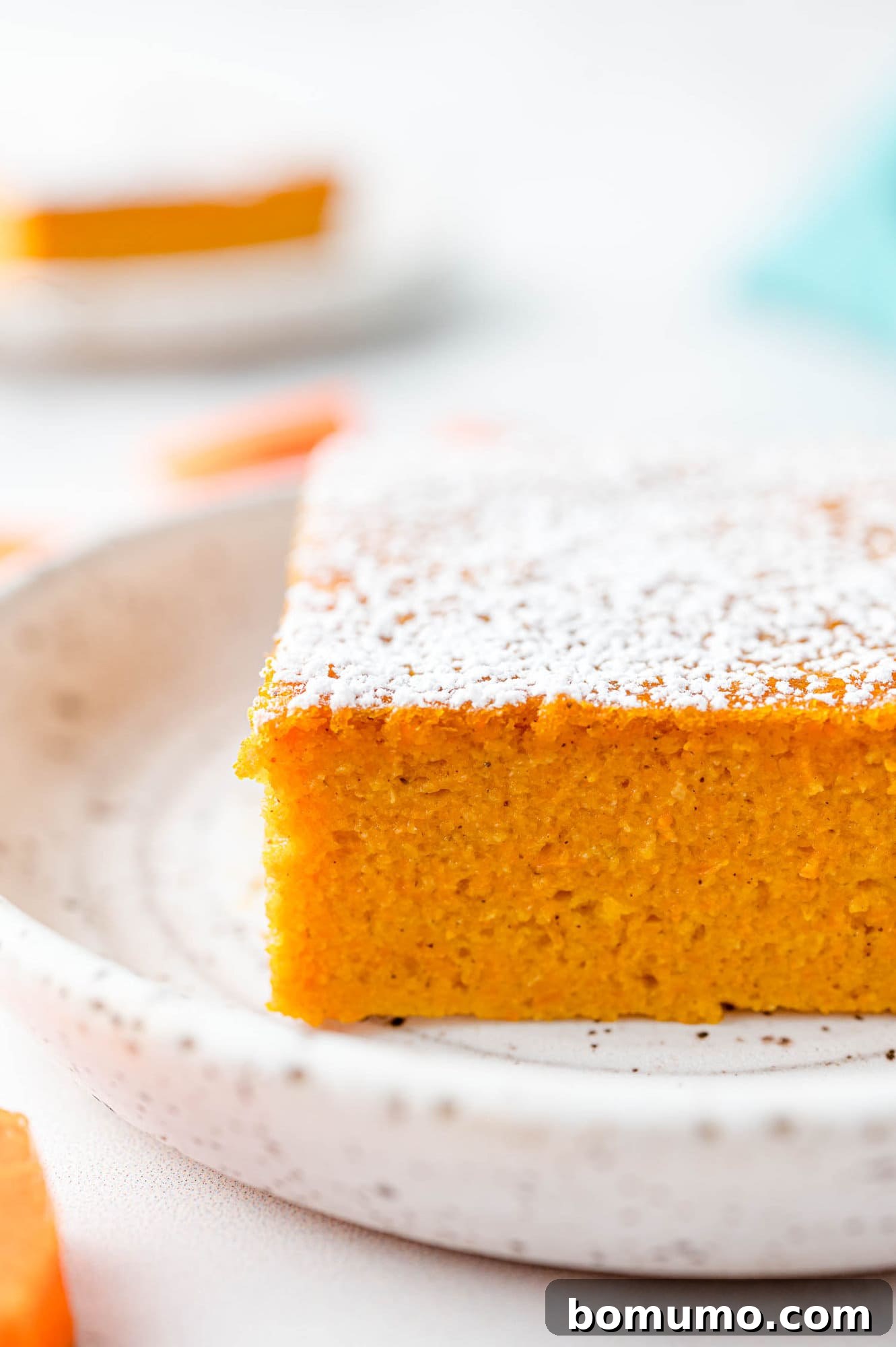 A side profile view of a slice of carrot soufflé, showcasing its moist and tender interior, served on a white plate.