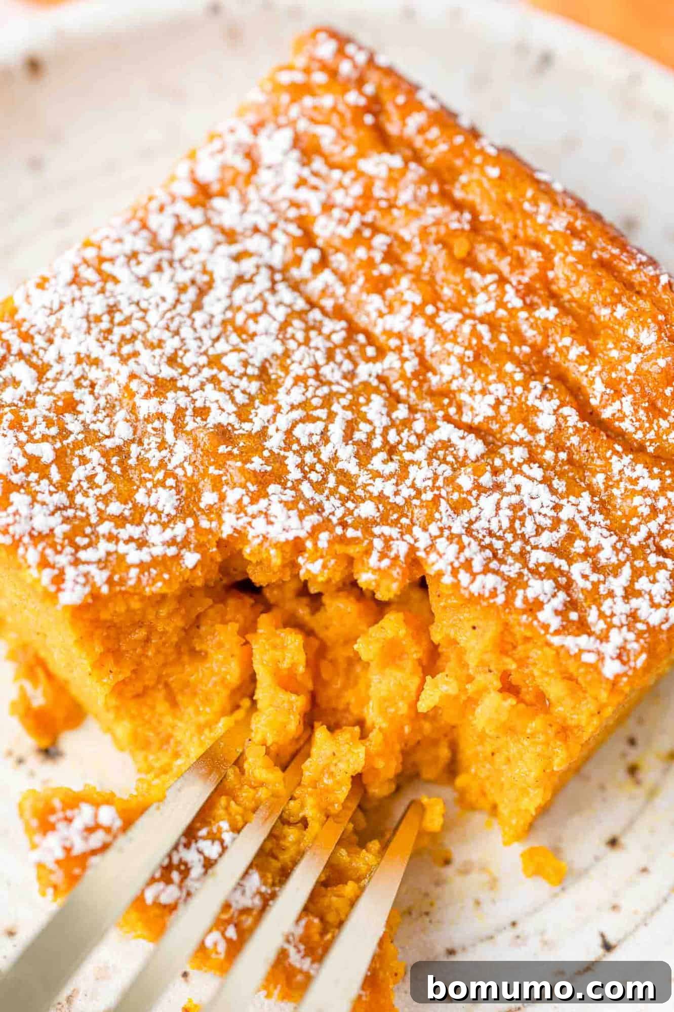 A close-up view of a slice of carrot soufflé on a white plate, with a fork removing a small portion, highlighting its soft texture.