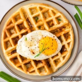 Overhead view of a savory waffle topped with a perfectly fried egg, ready to be enjoyed.