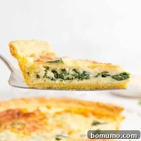 Spinach quiche on a pie server, held above the rest of the quiche, showcasing its golden crust and creamy filling.
