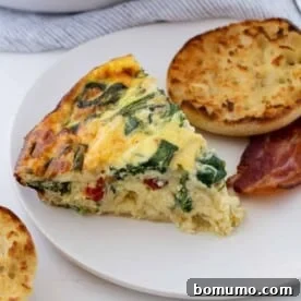 A slice of crustless quiche on a plate with an English muffin and bacon, illustrating a complete brunch plate.