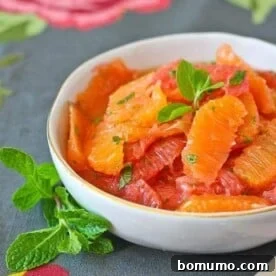 A shallow round white bowl containing a vibrant citrus salad, elegantly garnished with fresh mint leaves.
