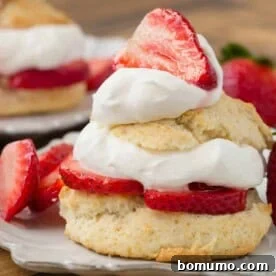 A beautifully layered strawberry shortcake on a white plate, showcasing fluffy biscuits, fresh strawberries, and whipped cream.