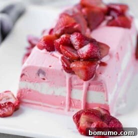 A stunning image of layered strawberry and vanilla ice cream terrine topped with roasted strawberries, arranged on a white rectangular plate.