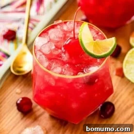 Bright red cocktail garnished with a cherry and a lime wheel.