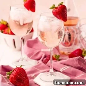 Two stemmed glasses with rose spritzers, garnished with strawberries.