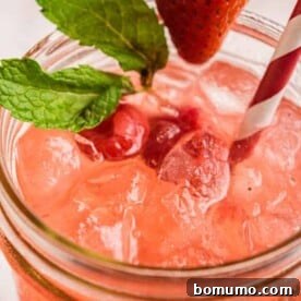 Close up view of a pink lemonade on ice, garnished with berries and fresh mint.