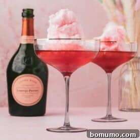 Two cocktail glasses filled with pink cotton candy and a pink liquid, placed next to a bottle of Laurent-Perrier champagne on a pink surface.