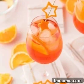 An light orange aperol spritz in a wine glass garnished with orange peel cut into the shape of a star.