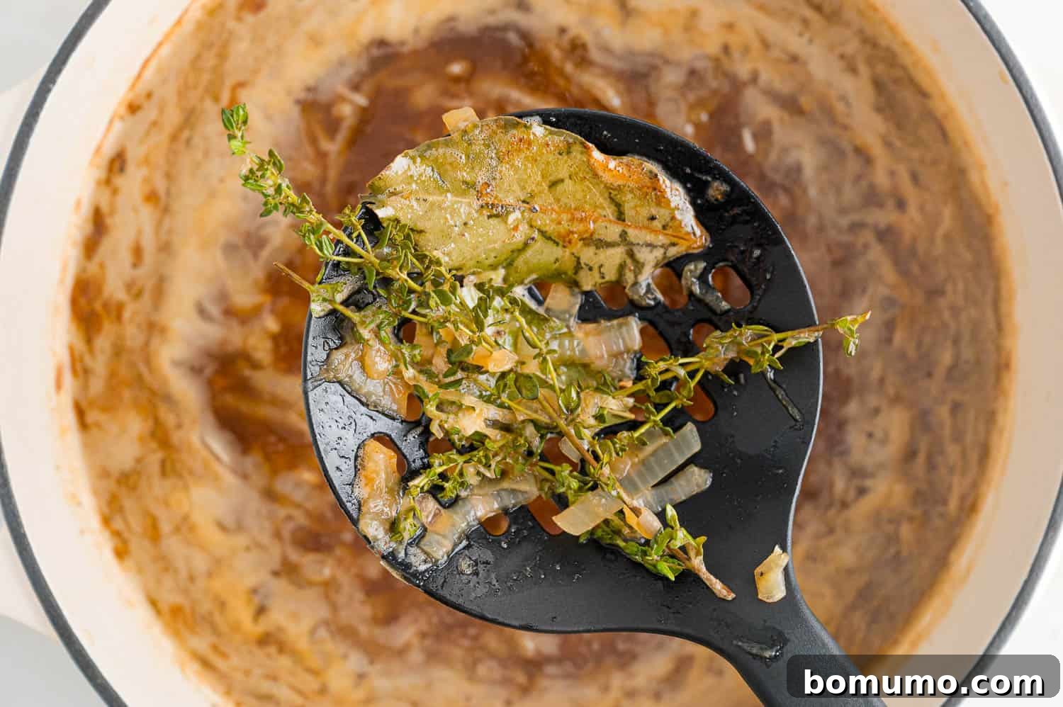 Removing thyme sprigs and bay leaves from the finished French onion soup.
