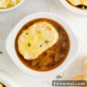 French onion soup in white bowl with bread and cheese topping.