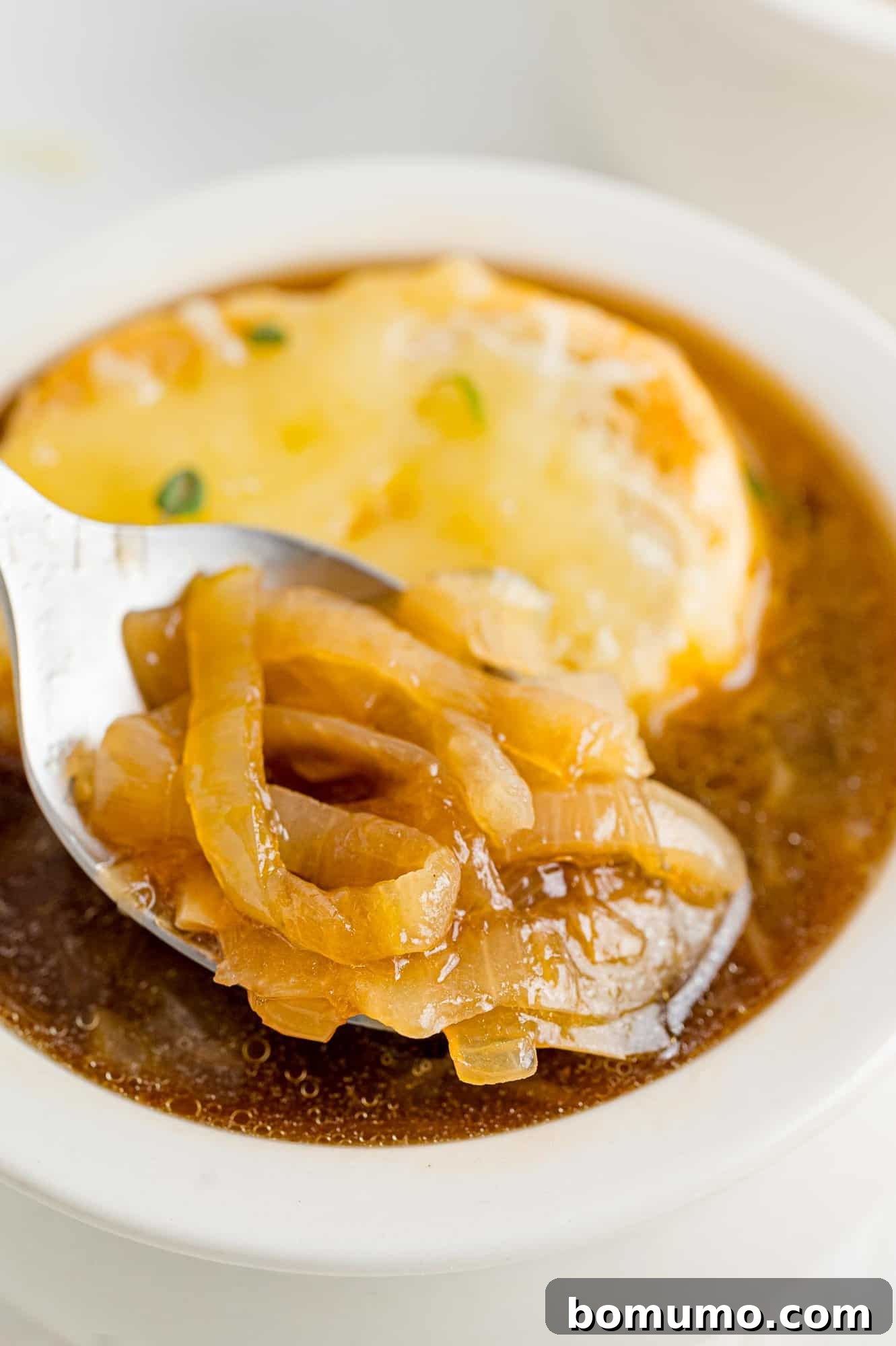 A spoonful of homemade French onion soup, showcasing the rich broth and soft onions.