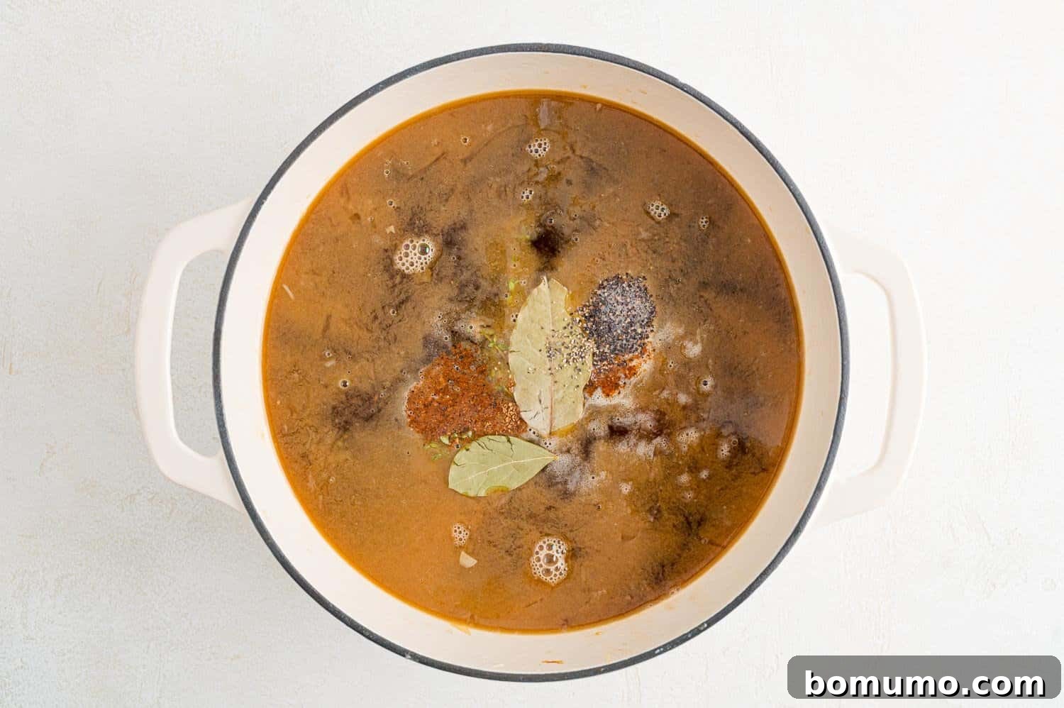 Beef broth, herbs, and bay leaves added to the caramelized onions and deglazed pan.