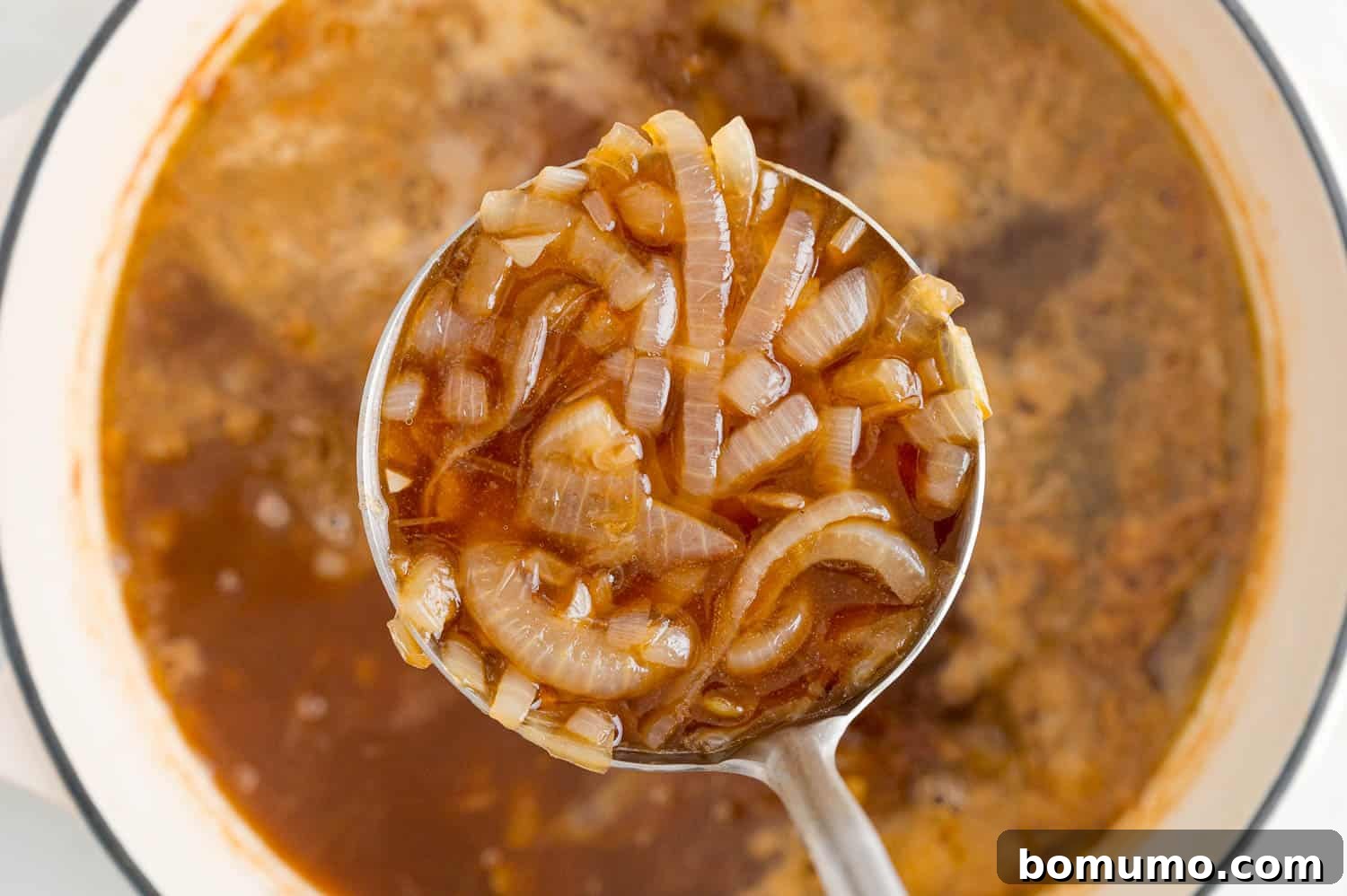 French onion soup being ladled, showcasing its rich, deep color.