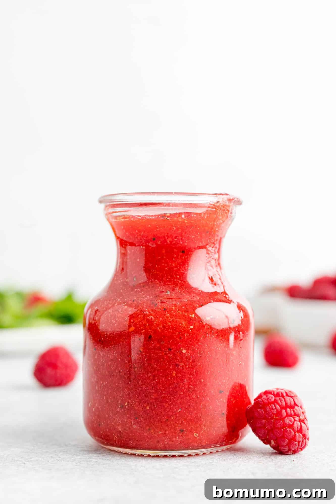 Fresh raspberry vinaigrette in a small container with fresh raspberries nearby, embodying summer's vibrant flavors.