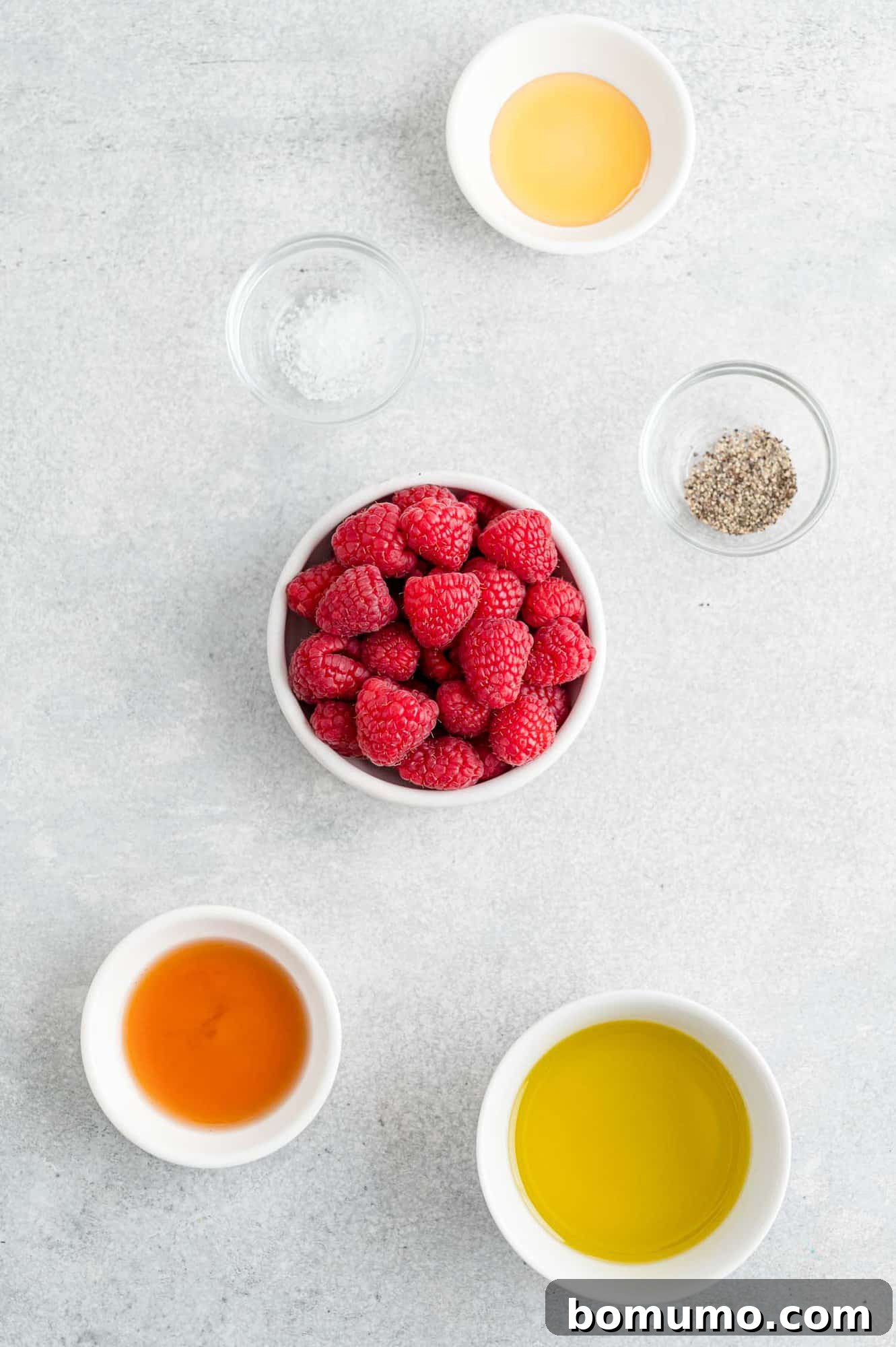 All the fresh ingredients needed for homemade raspberry vinaigrette, neatly arranged in separate bowls, ready for preparation.