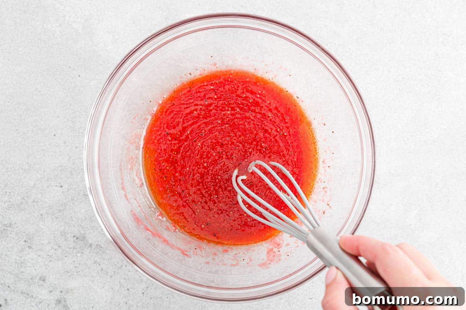 The raspberry vinaigrette dressing being actively whisked in a bowl, demonstrating the emulsification process.